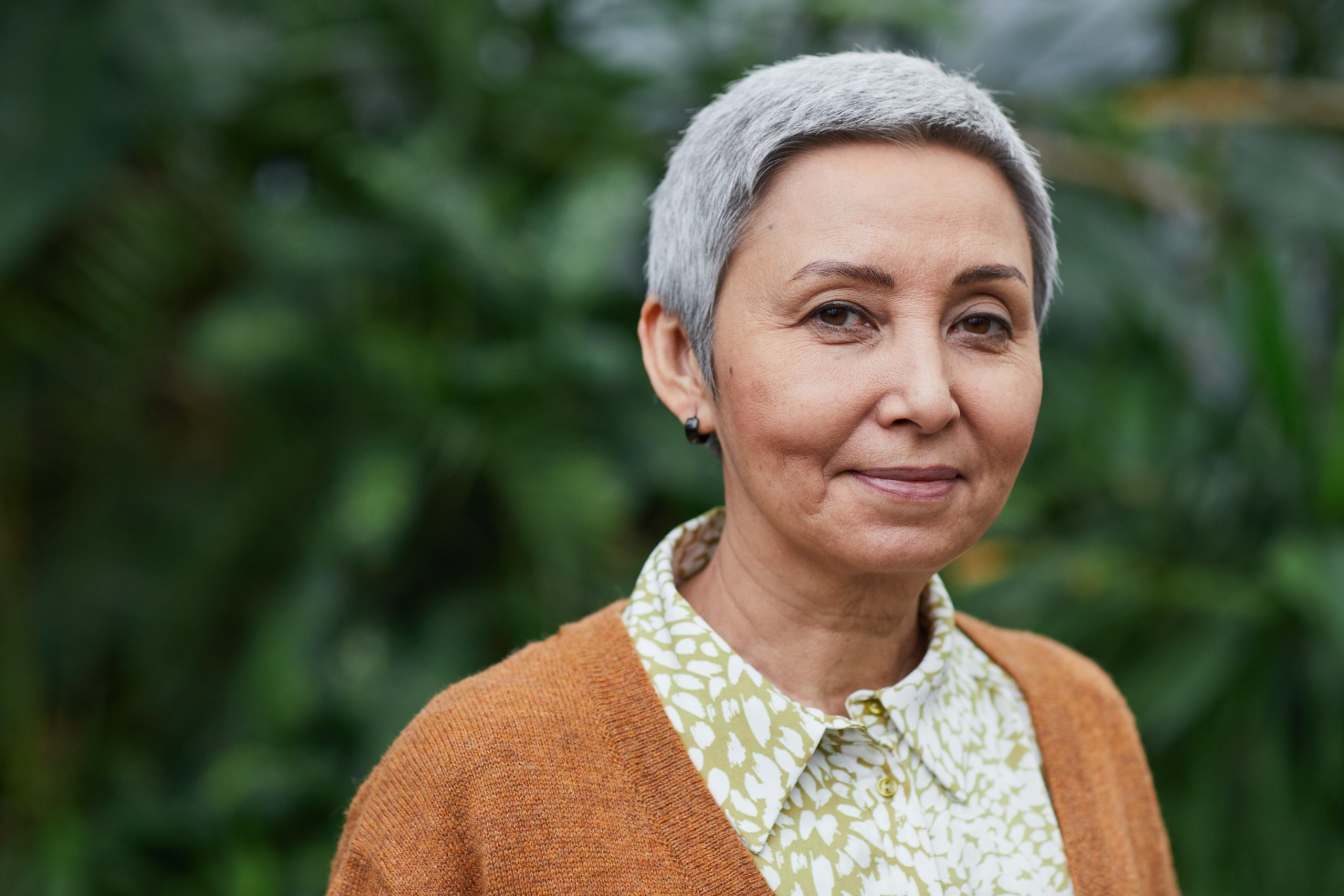 Eldre kvinne med kort grått hår står foran grønne planter